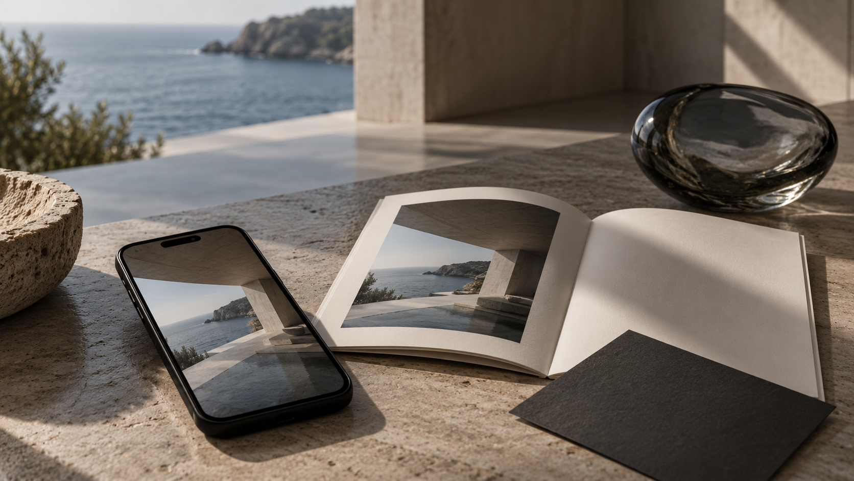 Teléfono y publicación editorial con imágenes de una residencia frente al mar sobre una mesa de piedra.
